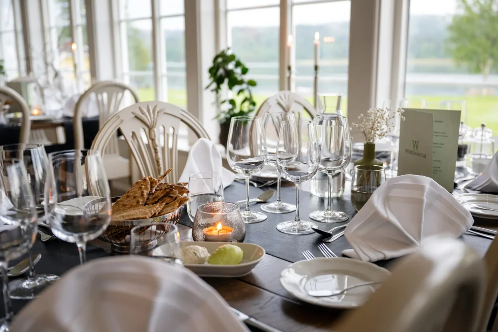 Dukat restaurangbord med glas, servetter och utsikt över sjön.