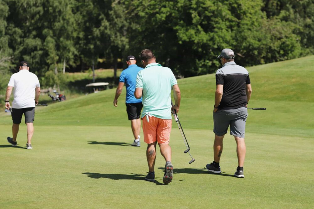 Fyra män går över golfbanan med klubbor i händerna.