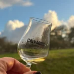 En hand håller ett glas calvados på Wiredaholm med gräsmatta i bakgrunden.